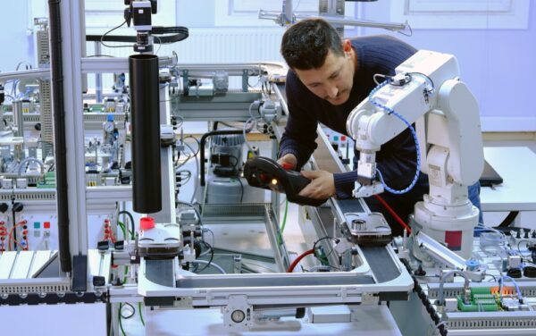 Man is programming robotic arm with control panel which is integrated on smart factory production line