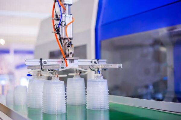 Stack of polypropylene food containers on conveyor belt of automatic plastic injection molding machine with robotic arm