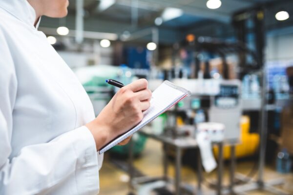 Young happy female worker in factory writing notes about water bottles or gallons before shipment