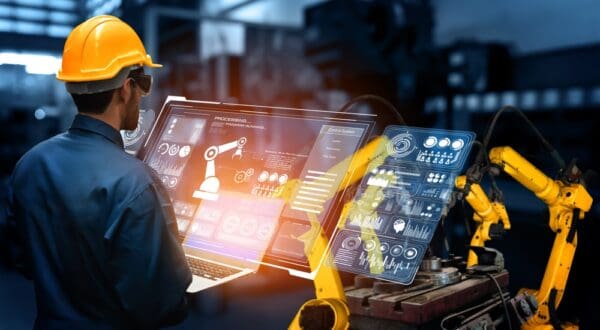 An engineer wearing a hard hat interacts with a digital interface to control robotic machinery